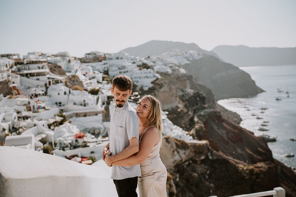 Couple embracing on white terrace with classic Santorini village and caldera views.