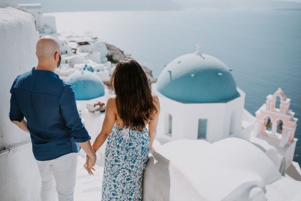 A couple admires the stunning Aegean Sea view from Santorini's white-washed pathways.