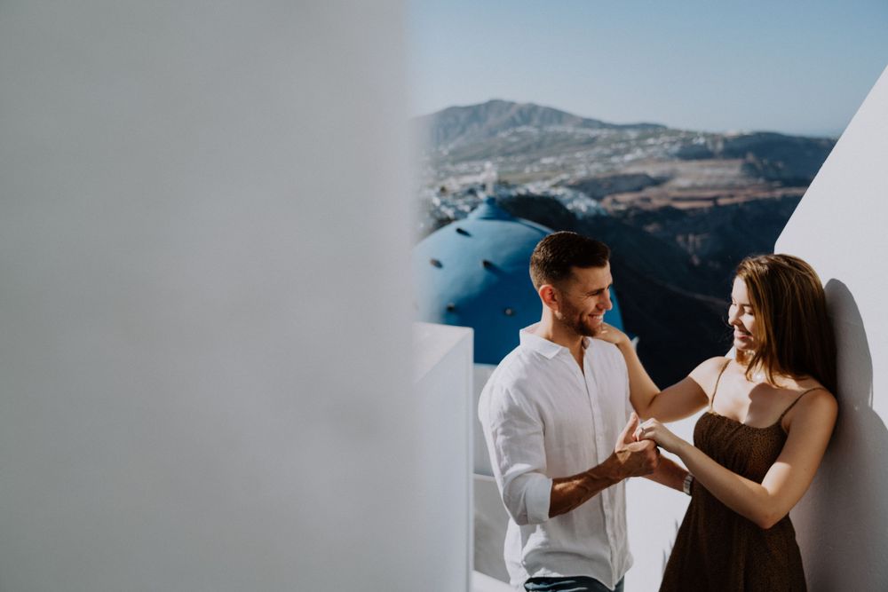 Intimate moment against white walls with Aegean Sea vista in background.