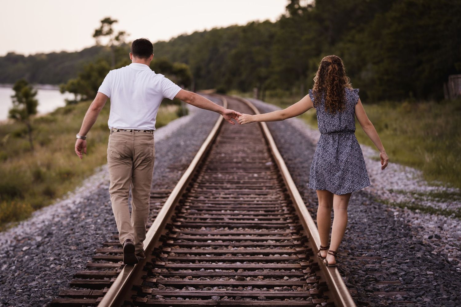 A couple balancing on railroad tracks while holding hands in a romantic pose at sunset.