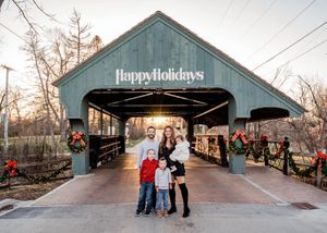 A holiday scene at a covered bridge decorated with 'Happy Holidays' sign and festive decorations.
