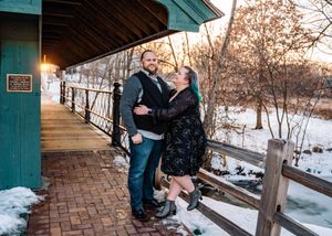 A couple embraces on a snowy covered bridge walkway during winter.