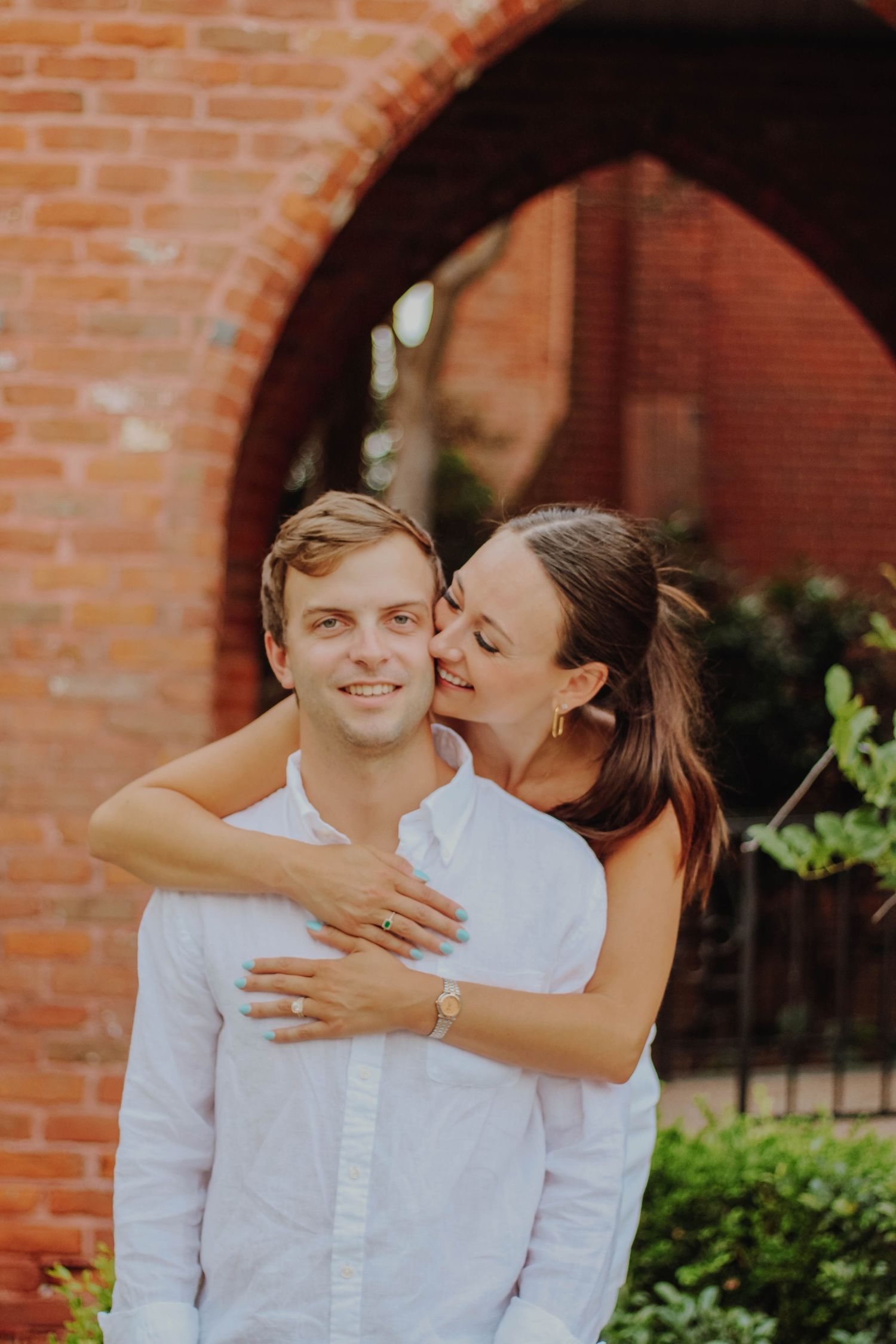Romantic couple embracing under brick archway in garden setting.