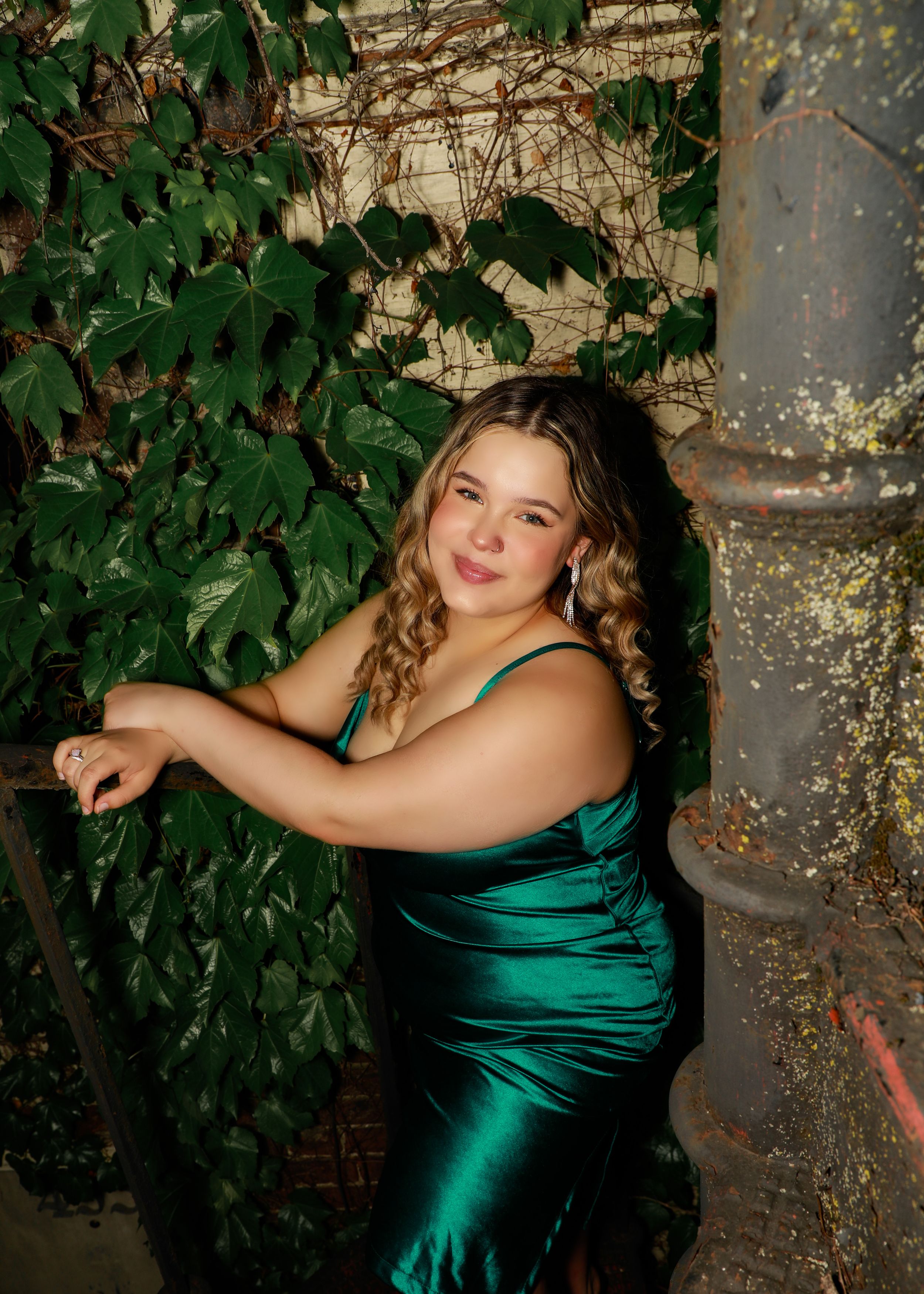 Elegant poses in emerald green dress against natural foliage backdrop.