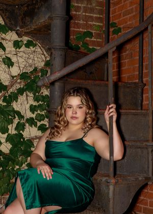 Fashion poses in a green dress against industrial brick and metal architecture.