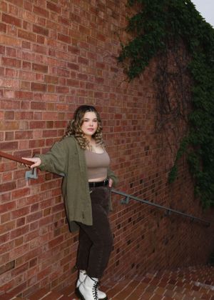 A casual fashion shoot against a brick wall featuring an olive jacket and white boots.
