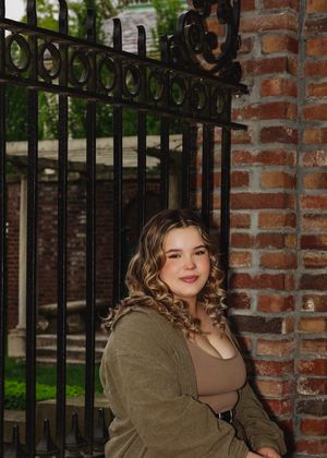 Portrait by ornate iron gate and brick column in casual olive outerwear.