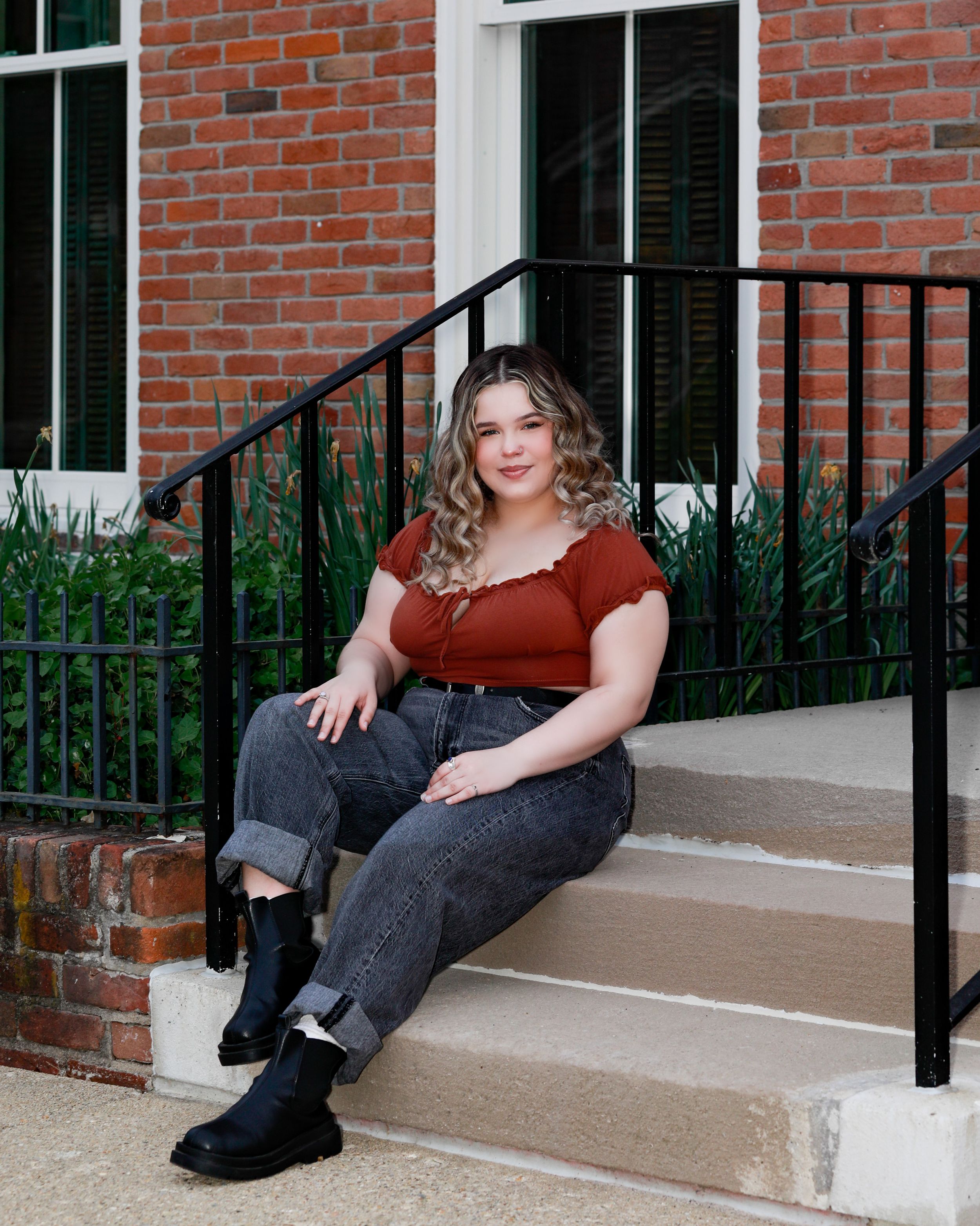 Relaxed portrait on concrete steps with brick wall and black railing.