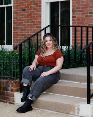 Relaxed portrait on concrete steps with brick wall and black railing.