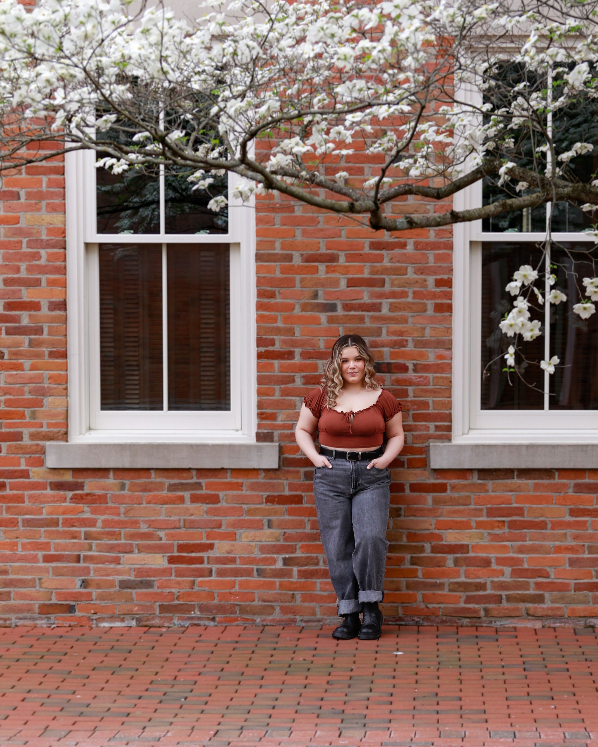 Spring portrait against brick wall with blooming cherry blossoms and white-trimmed windows.