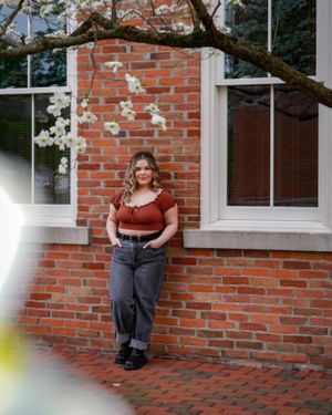 Portrait in rust-colored top against brick wall with cherry blossoms and windows.