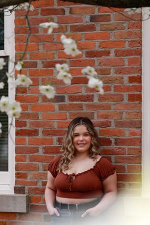 Portrait session against rustic red brick wall with white floral accents.