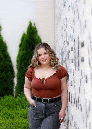 Casual portrait in rust-colored top against white wall with greenery.