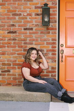 Casual portrait sitting on concrete steps by orange door and brick wall.