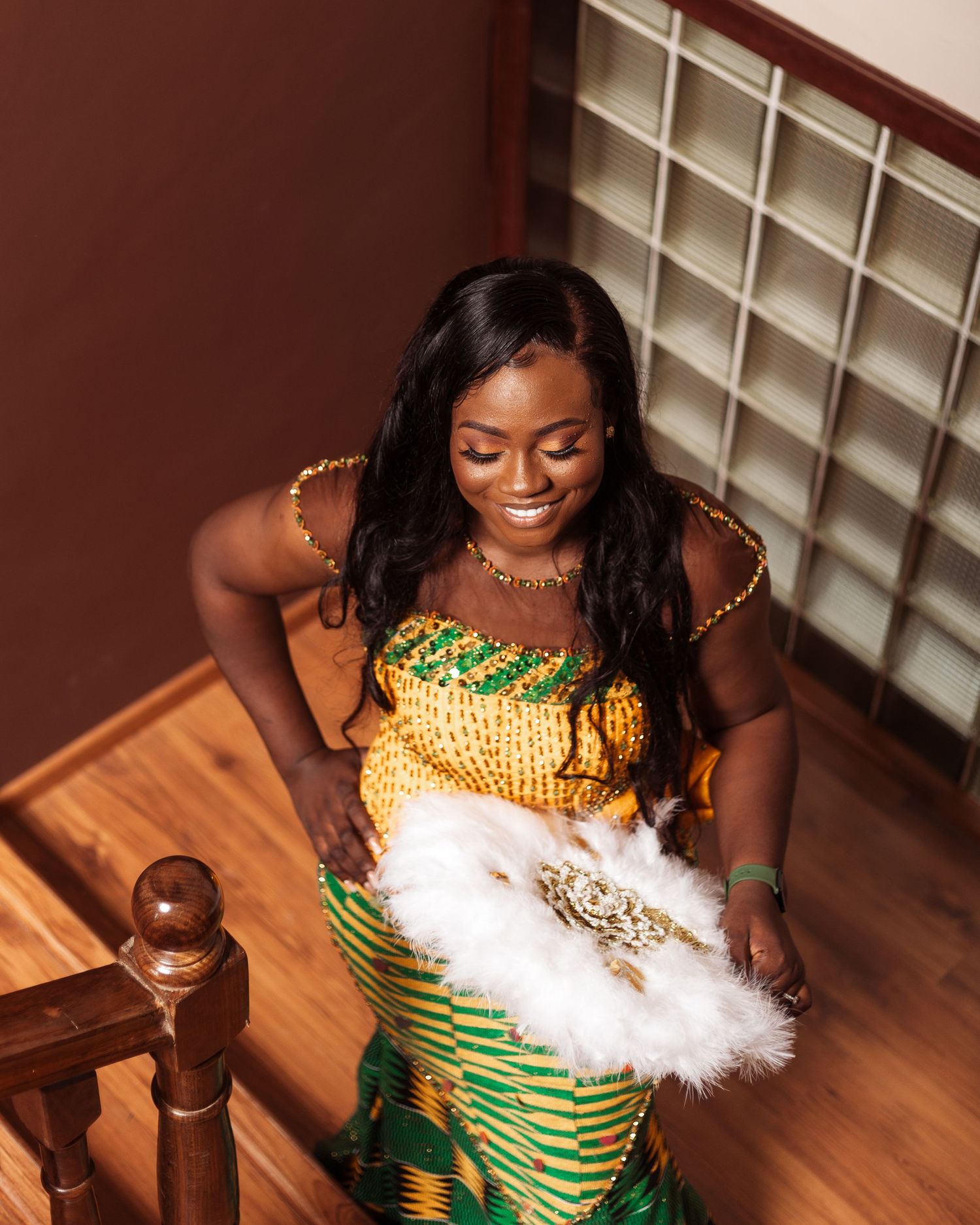 A joyful moment in a vibrant African print dress accessorized with a decorative white feather fan.