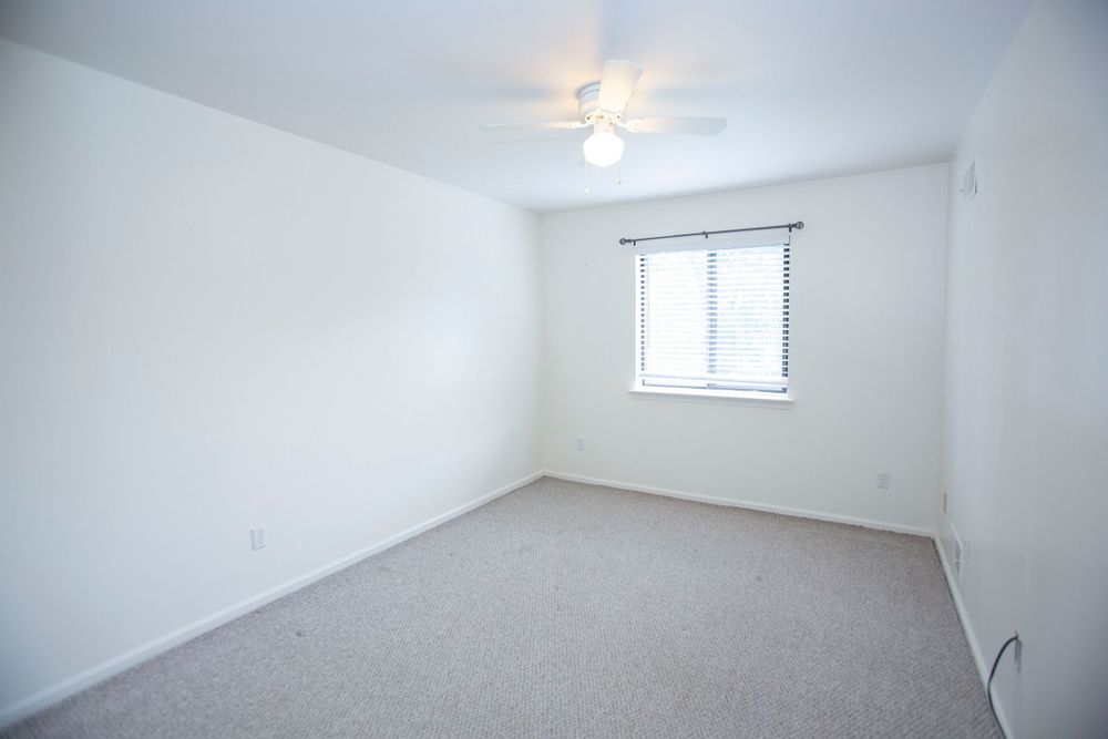 Empty bedroom with neutral carpet, white walls, ceiling fan, and a single window with blinds.