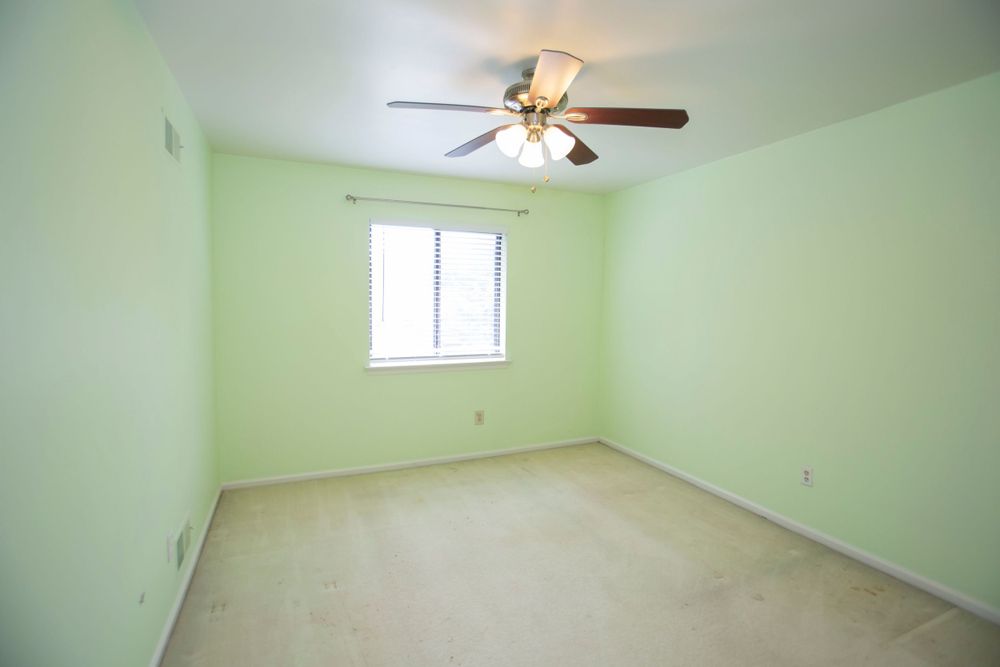 Empty bedroom with light green walls, carpet flooring, ceiling fan, and single window.