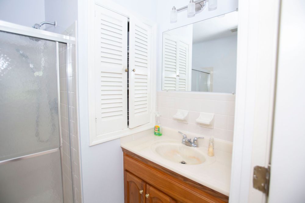 Clean bathroom with wood vanity, white sink, louvered cabinet doors, large mirror, and glass shower enclosure.