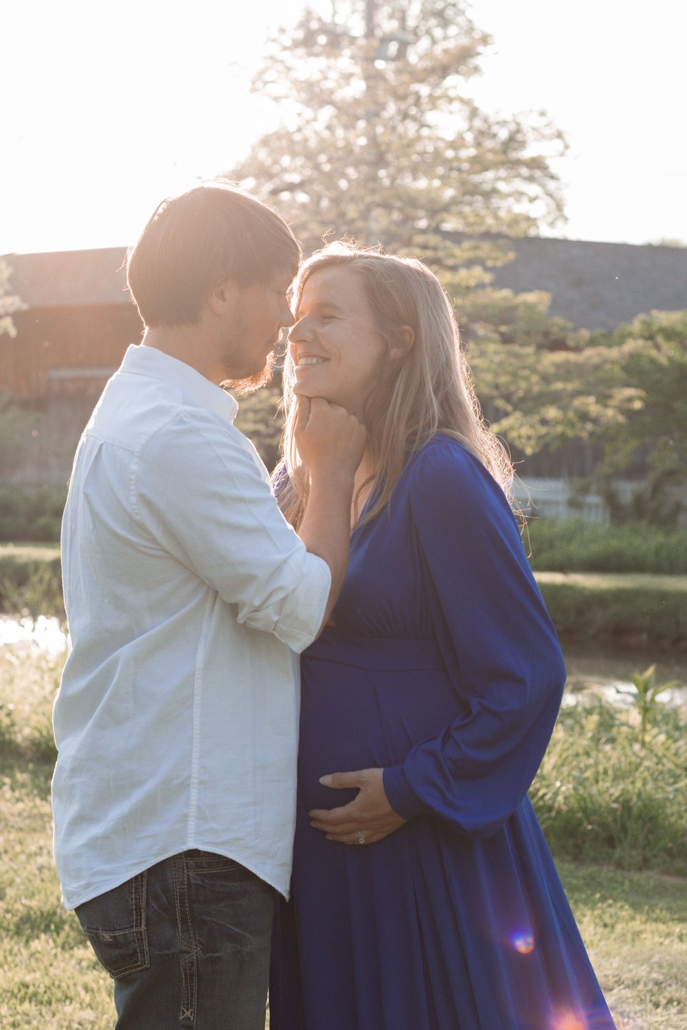 Intimate maternity portrait with couple in white and blue against sunset.