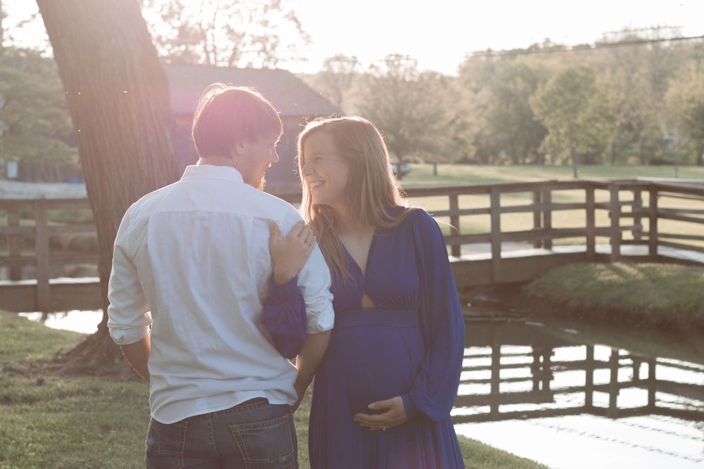 Couple sharing tender moment by wooden bridge during sunset maternity session.
