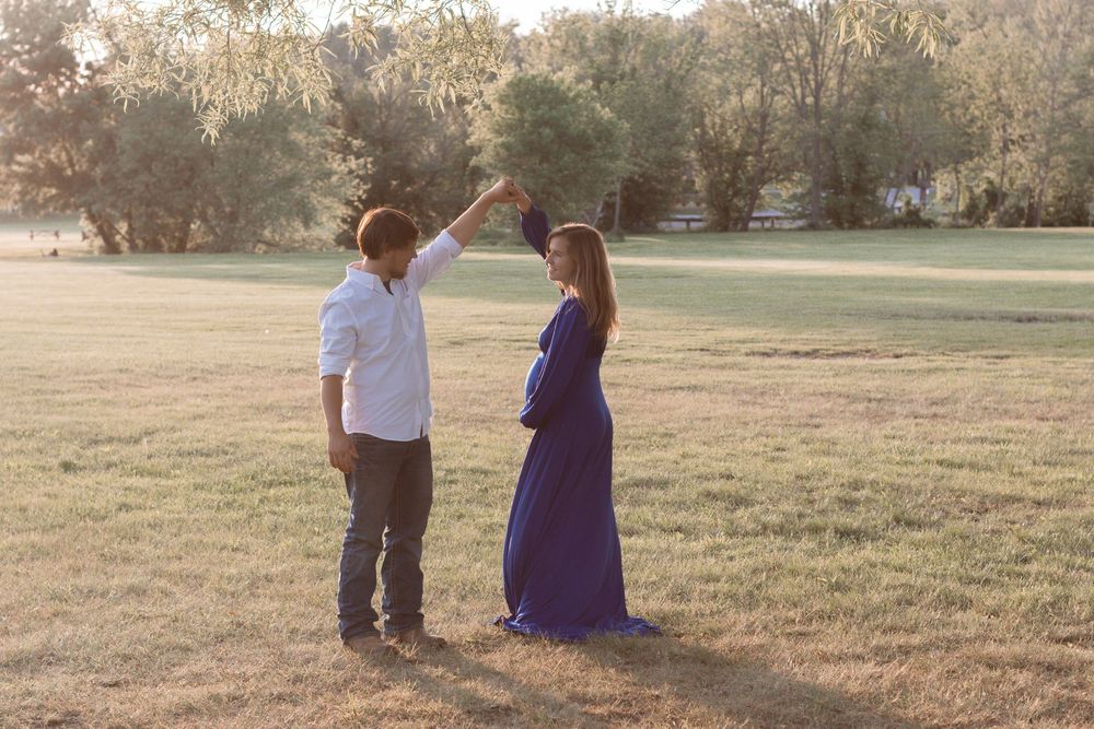 A couple poses together on grass during a romantic outdoor maternity session.