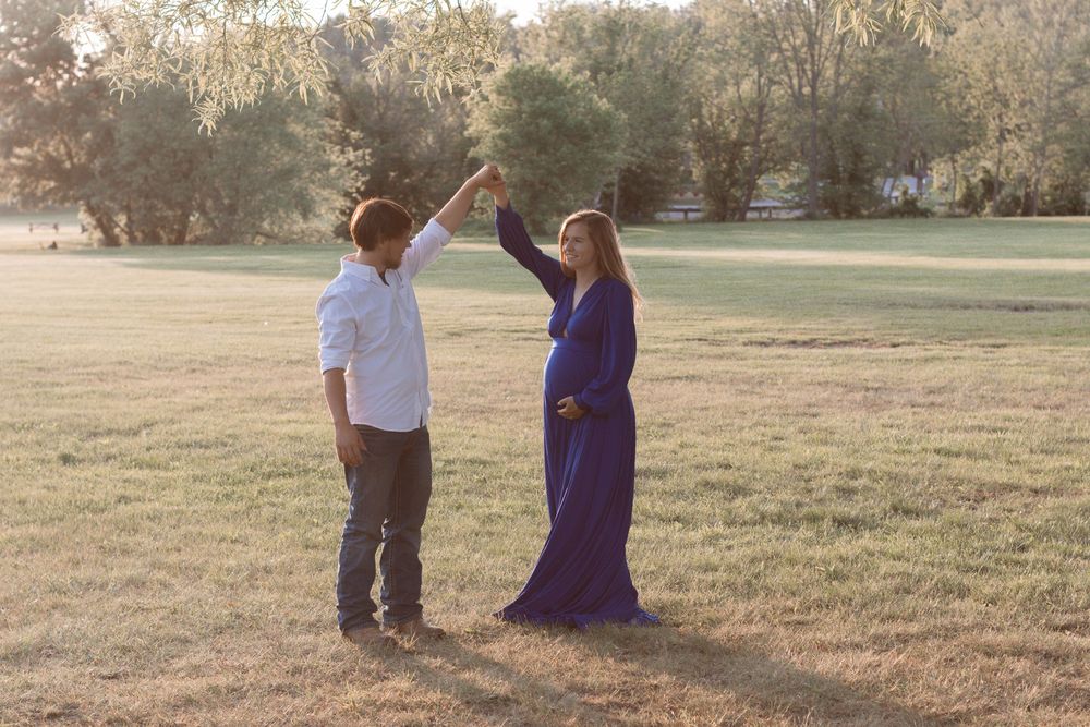A romantic outdoor maternity session features a couple in casual attire on grassy terrain.