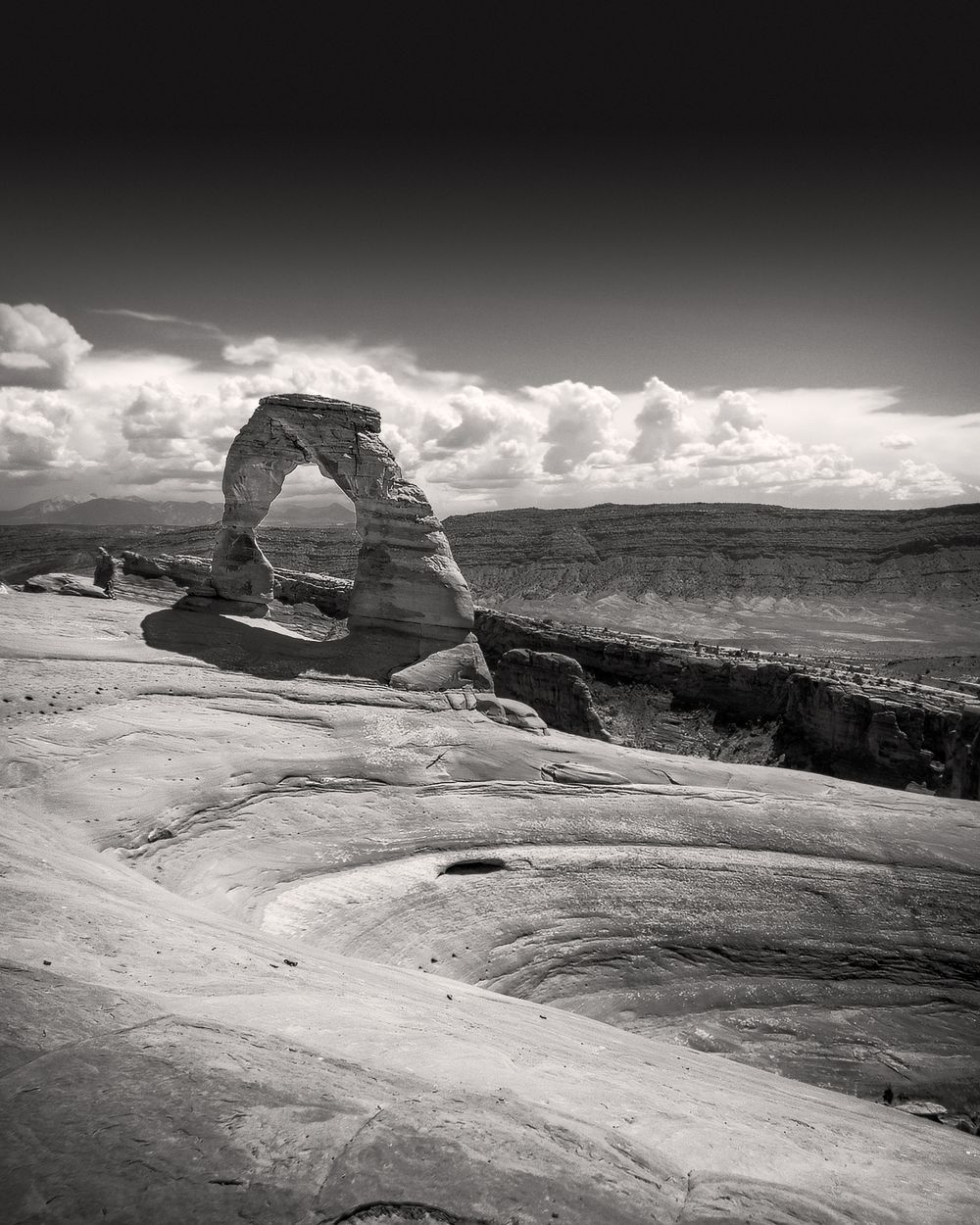 Delicate Arch stands majestically against white clouds in black and white photography.