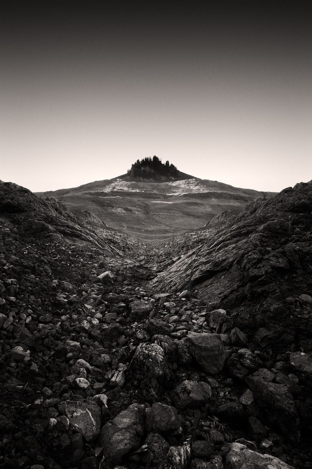 Rocky mountain landscape with jagged boulders leading to a distant peak against a dark gradient sky.