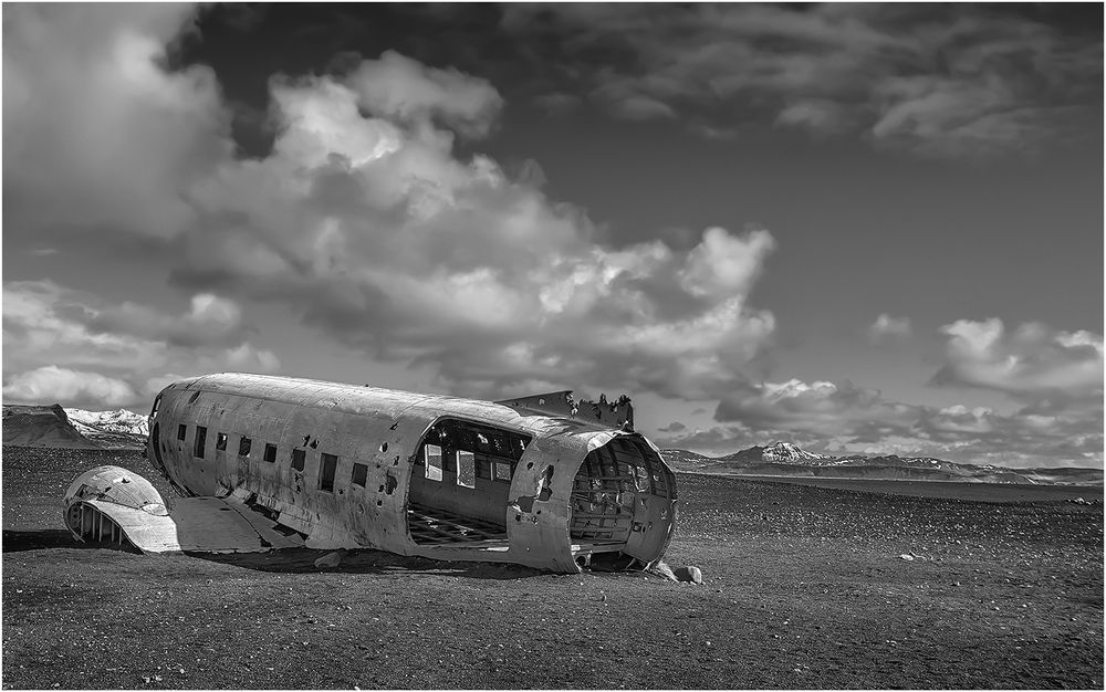 Black and white photo of abandoned airplane wreckage in remote landscape.