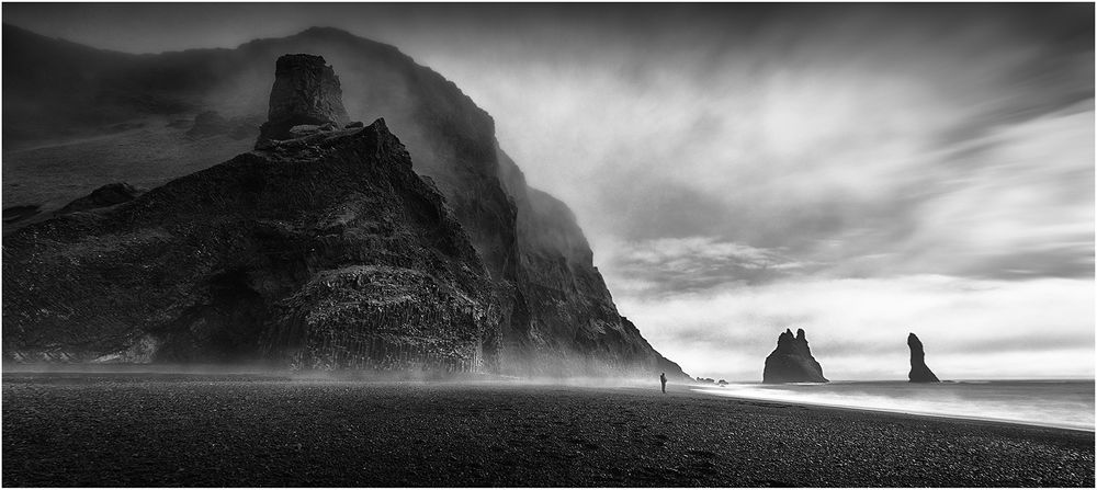 Dramatic black and white coastal landscape with towering cliffs and sea stacks under moody skies.