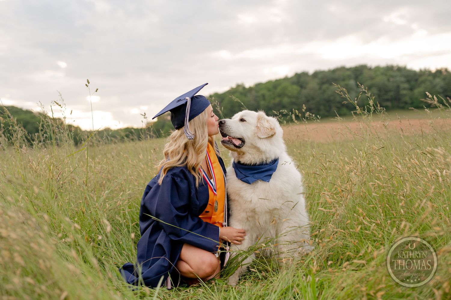 Graduate and white dog share a special moment together in a summer field at sunset.