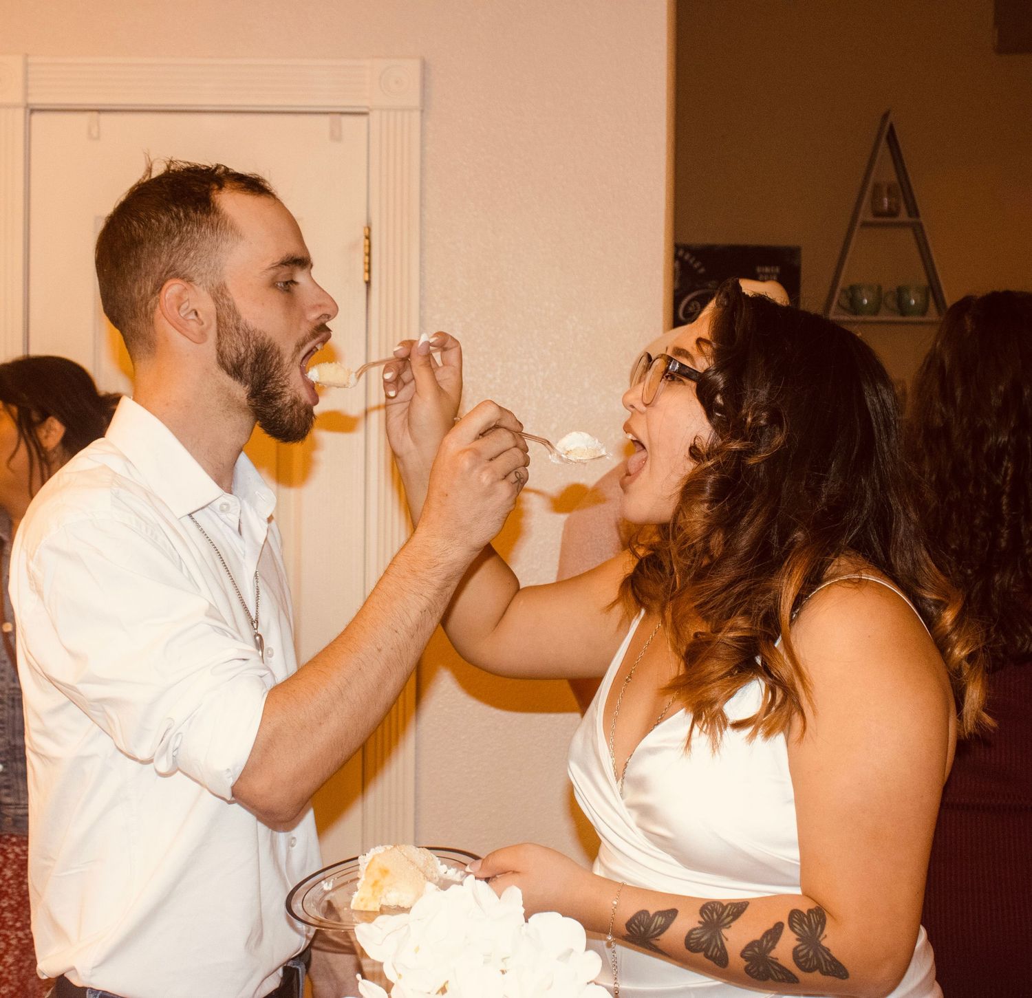 Bride and groom feed each other wedding cake at indoor reception celebration.