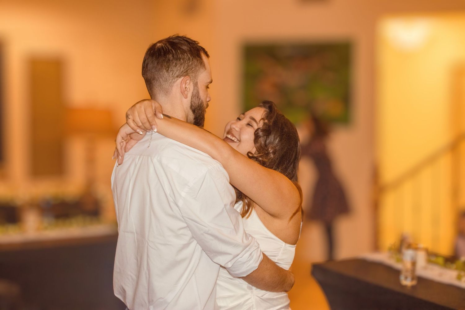 Couple shares a romantic slow dance together at their warm-lit indoor wedding reception.