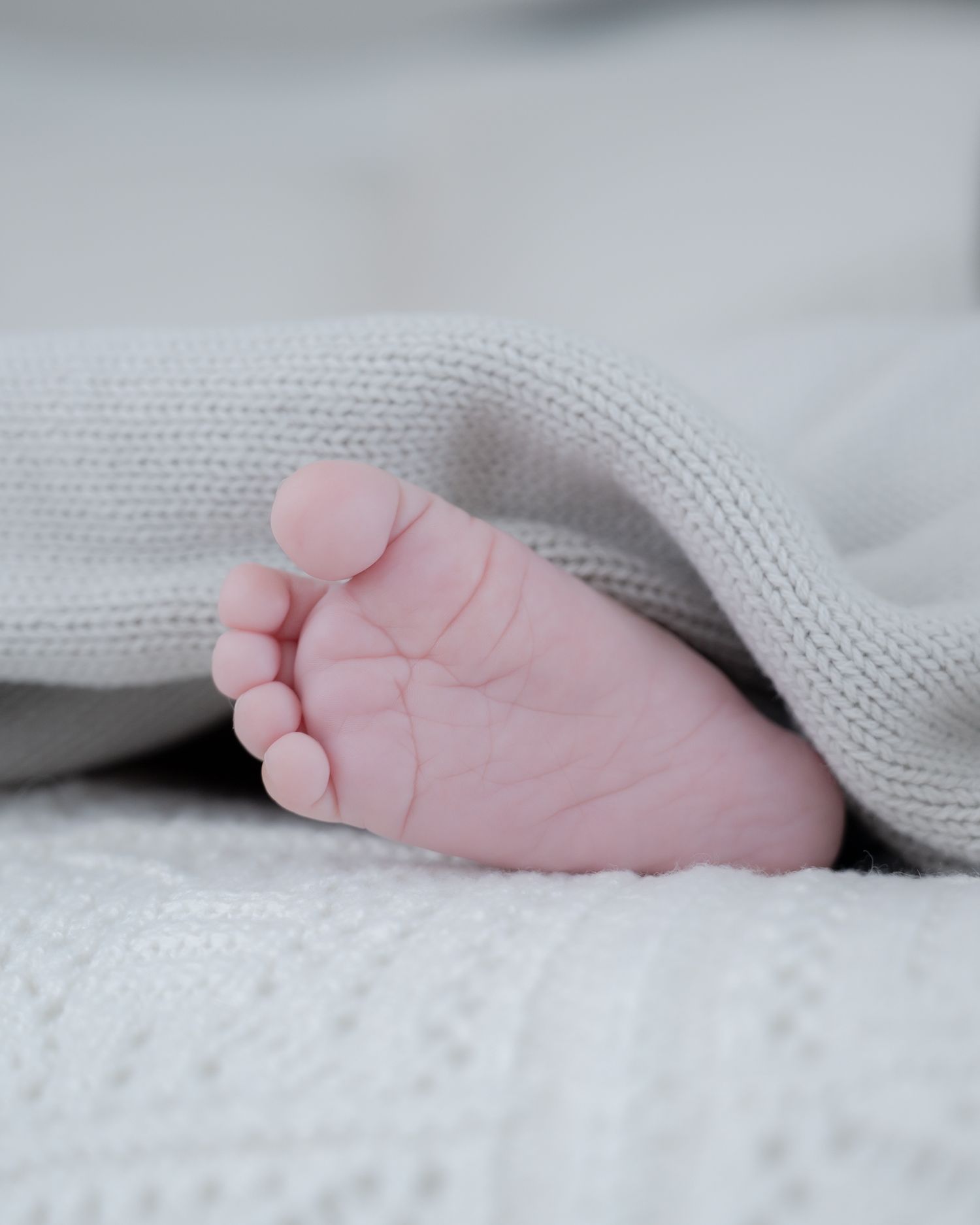 Tiny baby foot peeking out from under soft knit blanket.