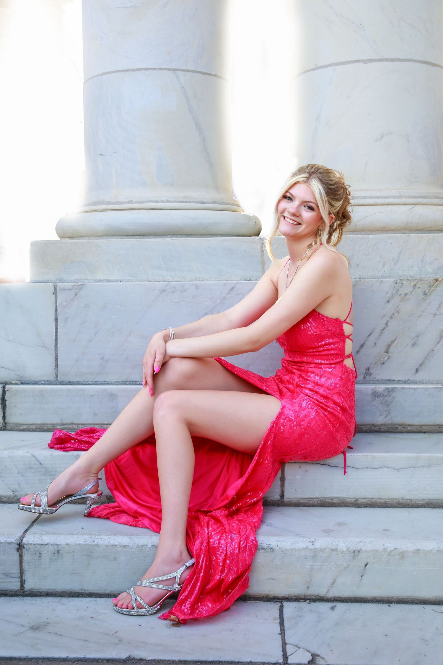 Glamorous red evening gown photographed against classic white marble columns.