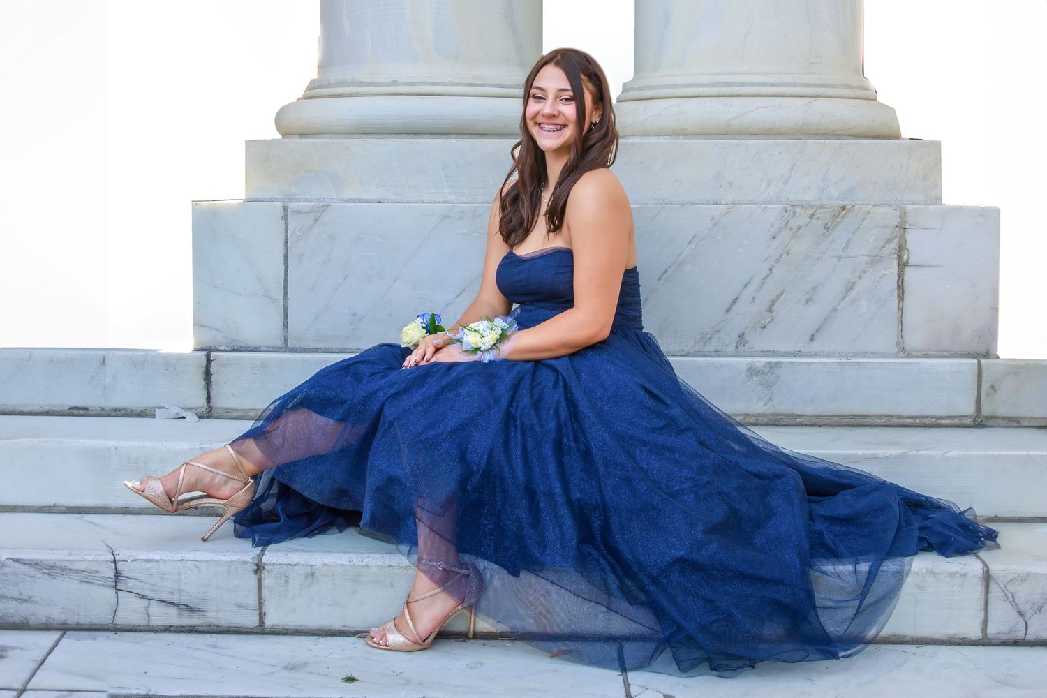 Navy blue tulle ball gown photographed on white marble steps with classical columns.