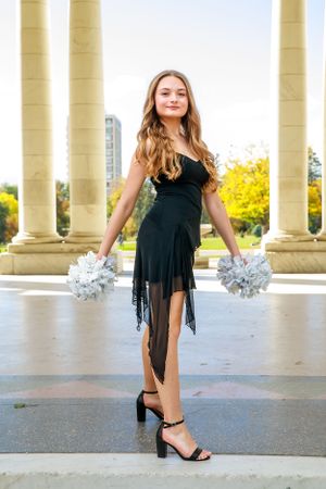 Black dress with silver pom poms photographed between yellow stone columns.