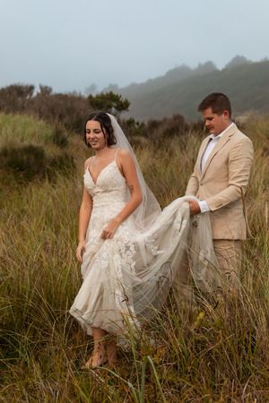 A couple poses in tall grass on their wedding day, wearing a lace gown and tan suit against misty mountains in Jacksonville.