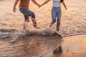 Couple splashing and playing in shallow ocean water at sunset, creating ripples in the golden light in Jacksonville North Carolina.