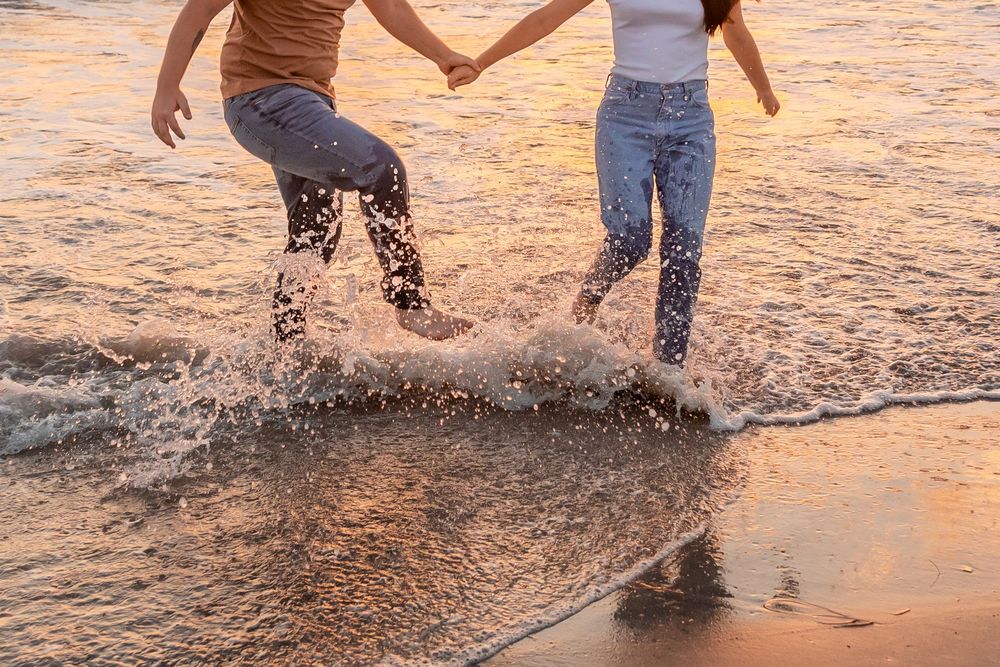 Couple splashing and playing in shallow ocean water at sunset, creating ripples in the golden light in Jacksonville North Carolina.