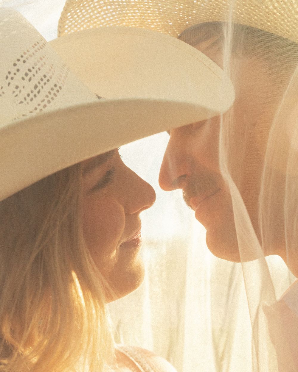 Silhouetted figures wearing cowboy hats stand in a row against bright sunlit background creating a dreamy atmosphere.