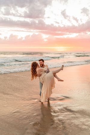 A couple dances in shallow ocean waves during a romantic pink sunset on a serene beach in Wilmington North Carolina