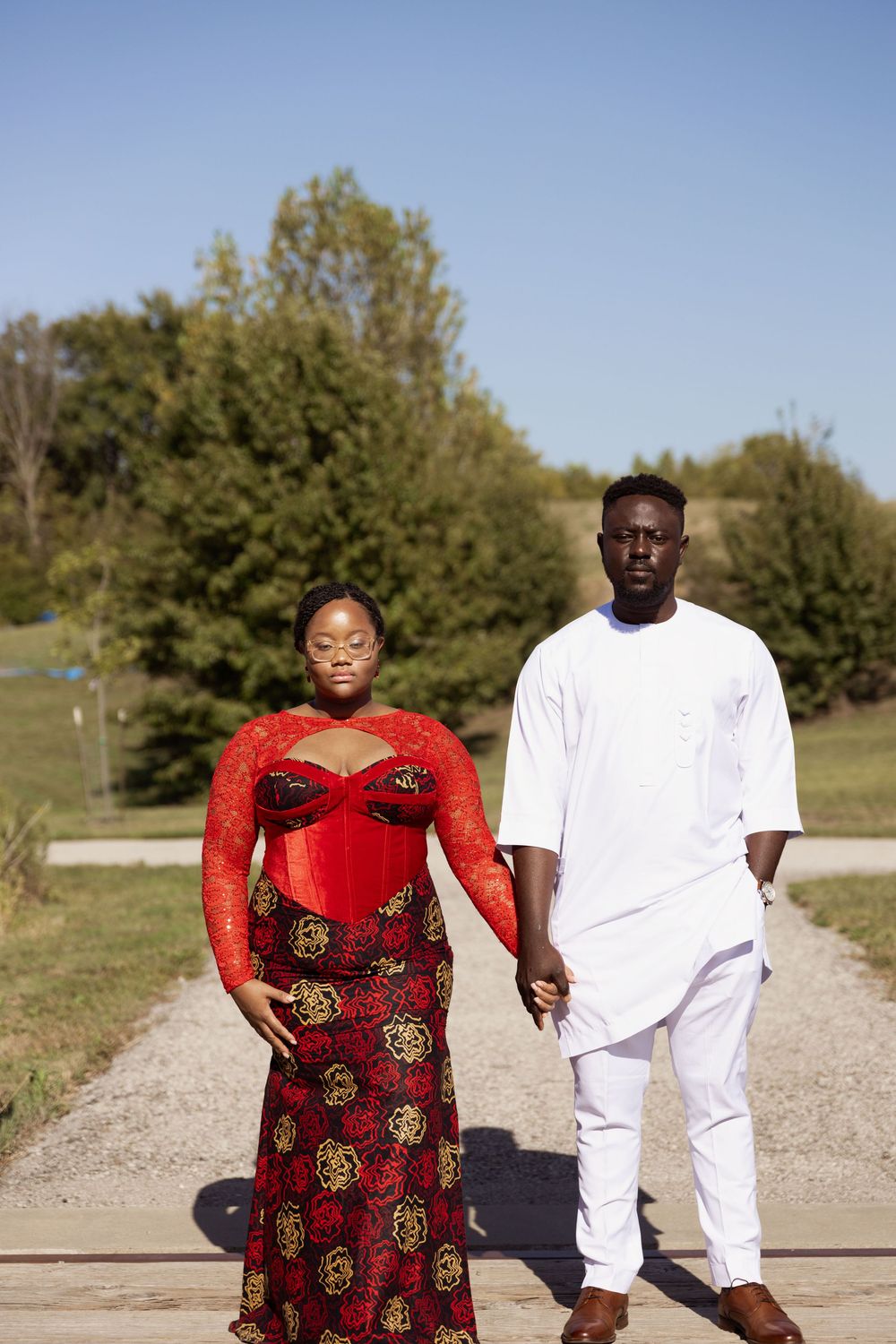 A couple walks together on a dirt path surrounded by green trees on a sunny day.