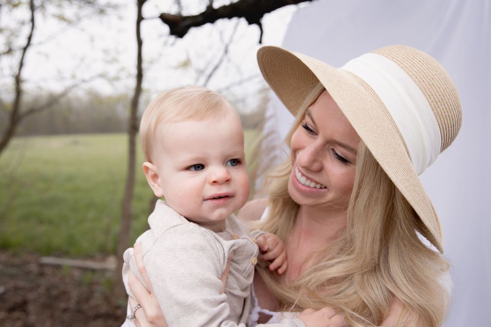 Happy parent in a beige sunhat holding a small child outdoors in a natural setting.