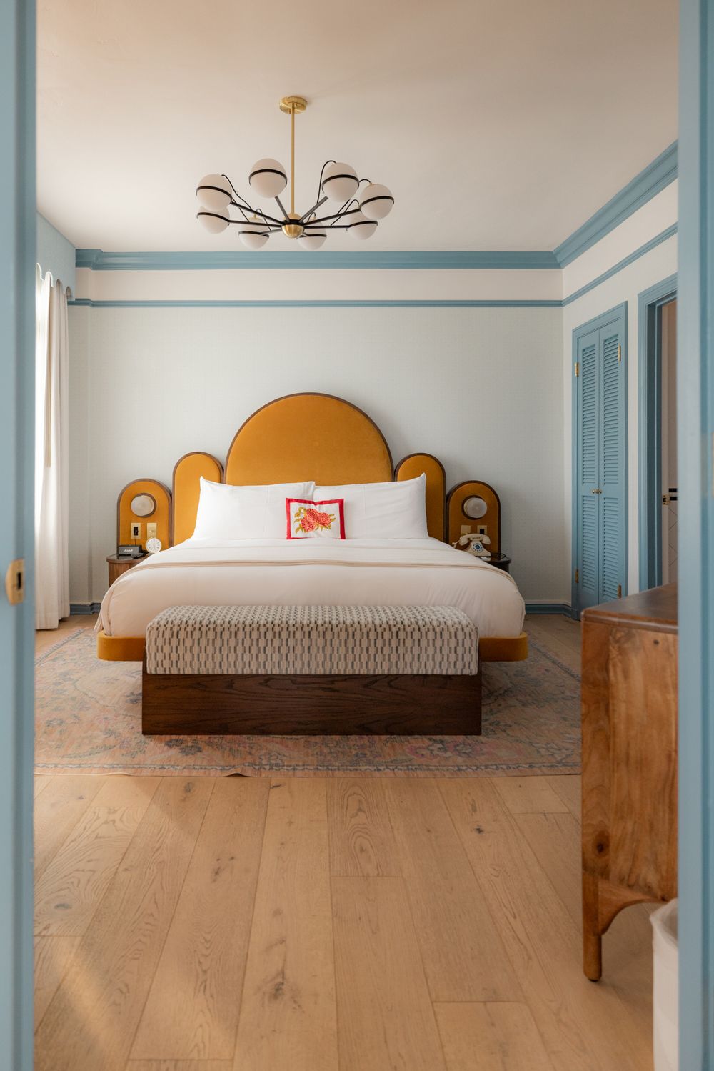 Modern hotel bedroom with light wood floors, white walls, blue trim, and minimalist decor features a king-sized bed.
