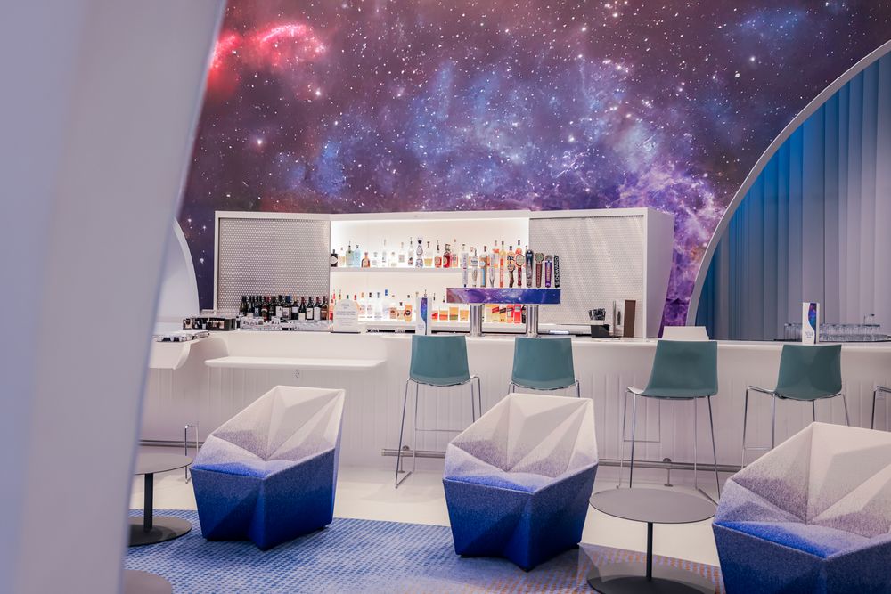 Futuristic bar lounge with cosmic galaxy ceiling, white bar counter, and geometric blue and white seating.