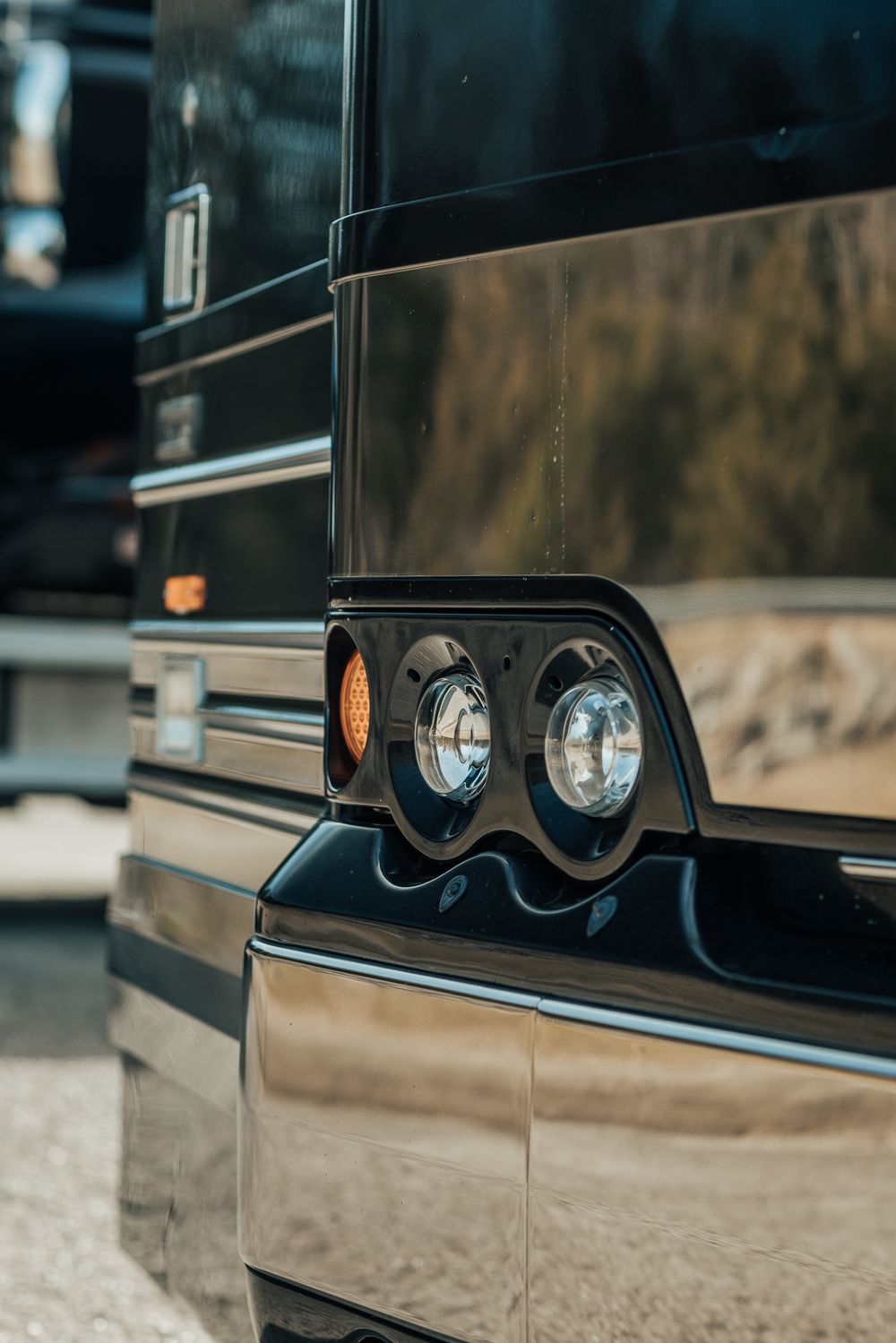 Close-up detail shot of dual headlights and chrome trim on a vintage brown RV motorcoach exterior.