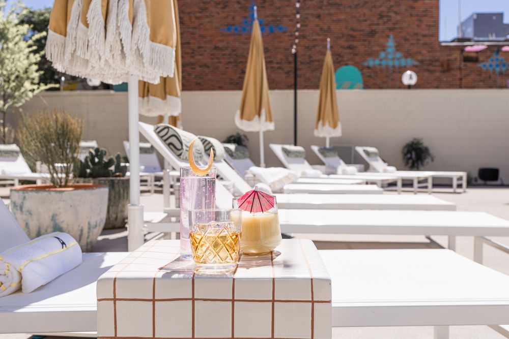 Poolside lounge chairs with umbrellas and refreshing drinks on a white tiled ledge at a luxury resort.
