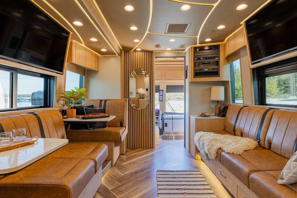 Interior view of a luxury RV showing modern brown leather seating, wood flooring, and elegant lighting fixtures.