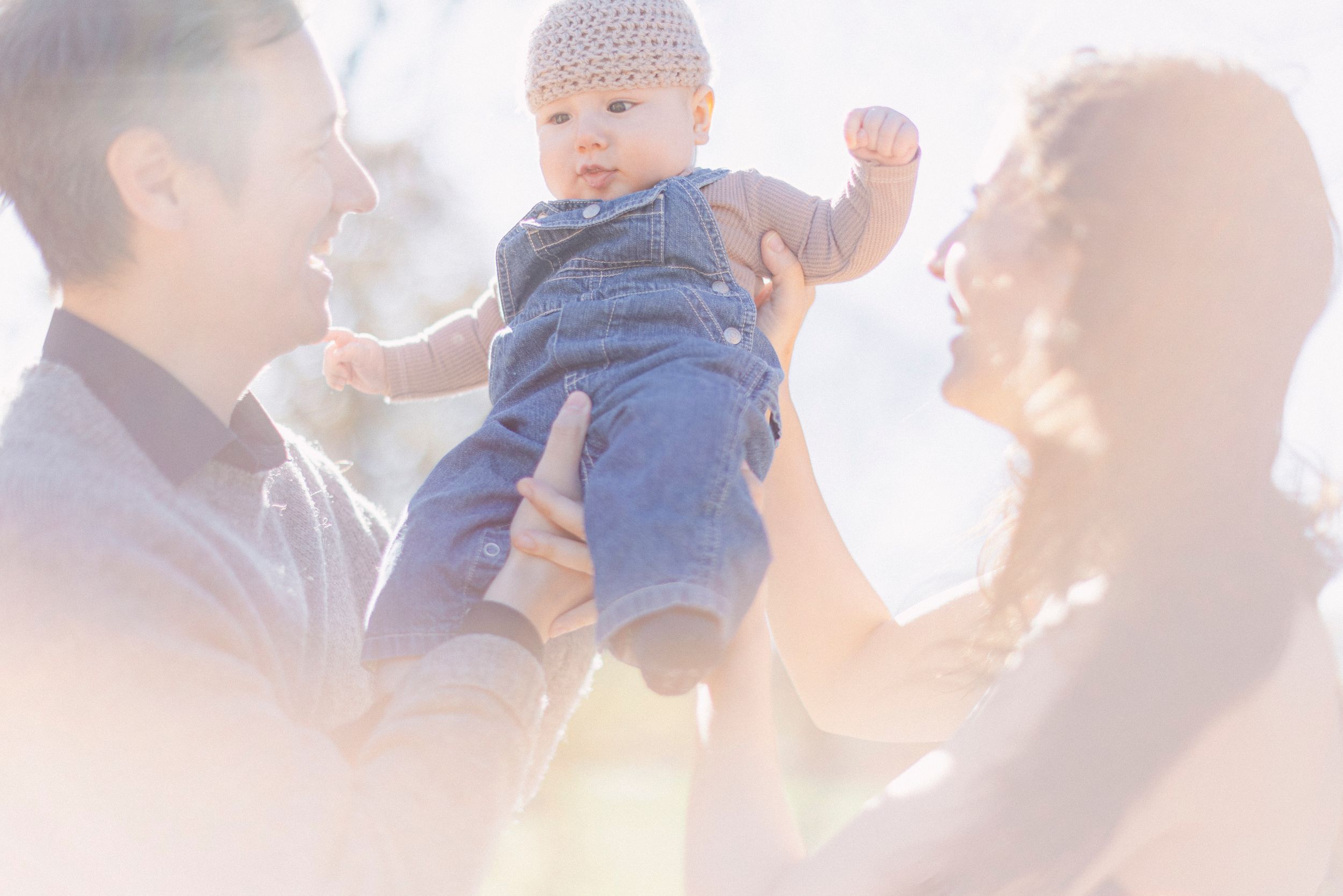 A family shares a lighthearted moment while lifting their baby in sunshine.